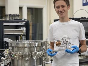 Jake Flowerdew, holding the previous IBEX Paul trap, stands next to the vacuum vessel containing the IBEX-2 trap in the IBEX lab at the Rutherford Appleton Laboratory.